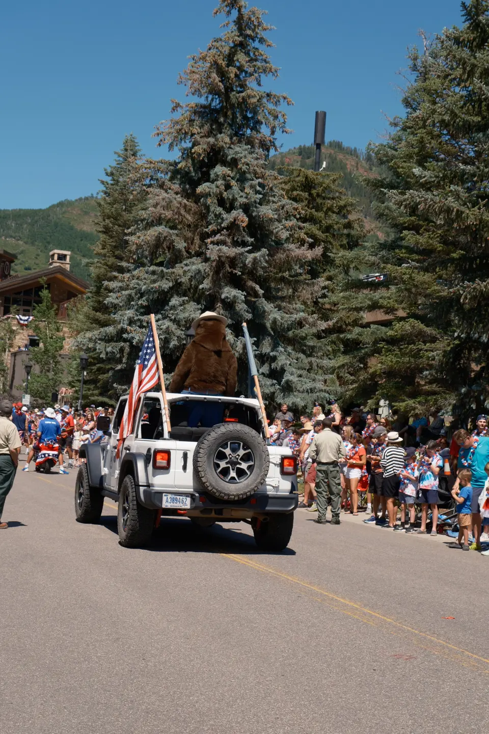 Jeep with an American flag in a Fourth of July parade, crowds along the route