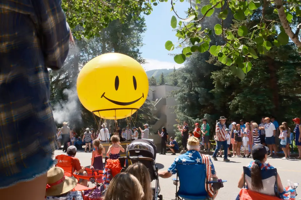 Giant smiley-face balloon floating over parade spectators in lawn chairs