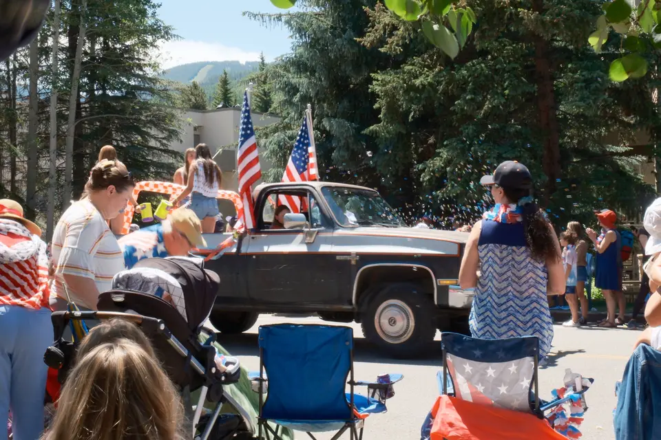 Vintage pickup flying American flags passes families watching the parade