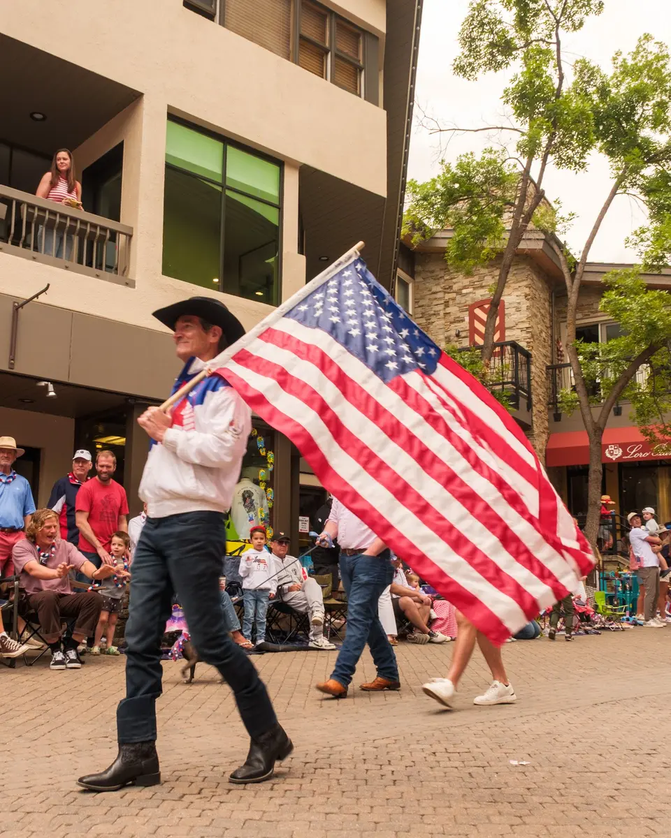 Man in a cowboy hat carrying a large American flag in the parade