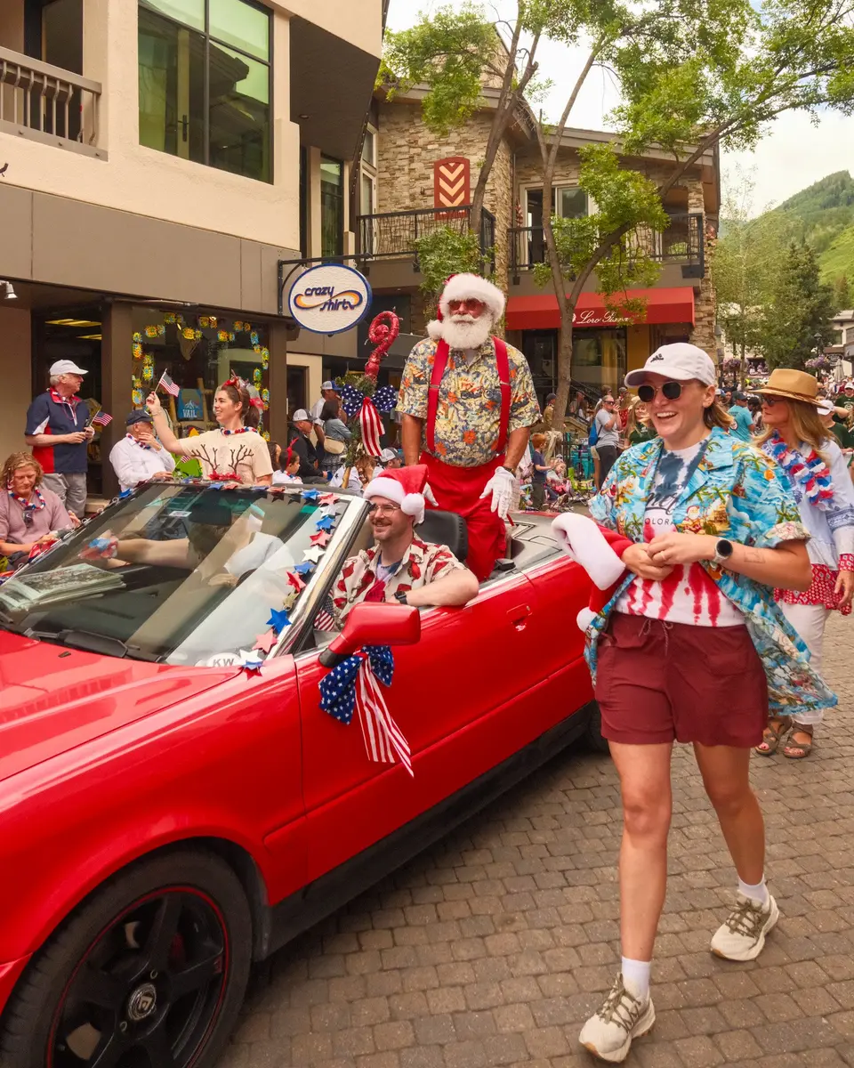 Santa in a red convertible with a parade walker in a flag shirt