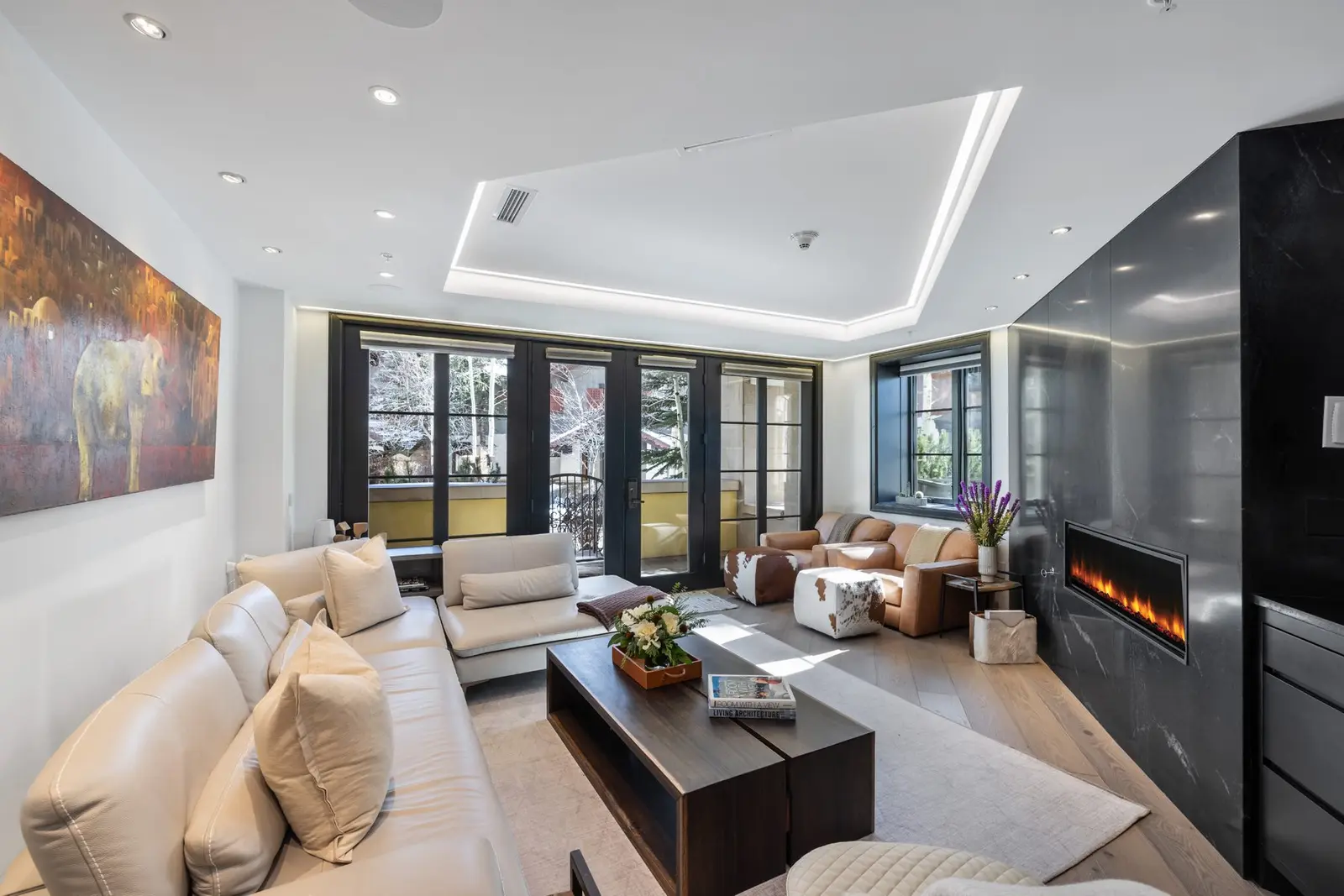 Modern living room with a fireplace on a dark marble wall and large windows onto snow-covered trees