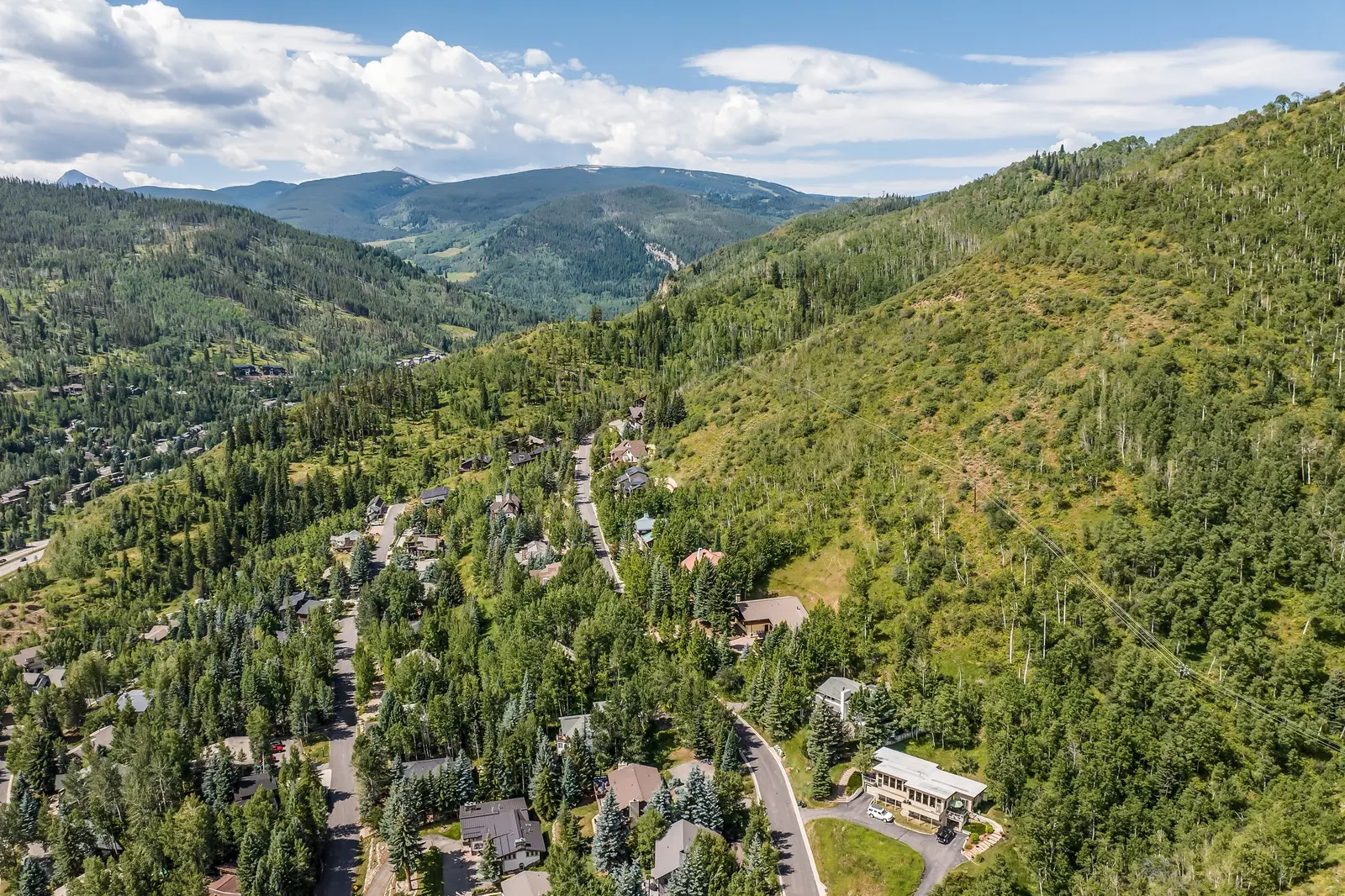 Aerial view of a mountain community among green forests, winding roads and houses under a blue sky